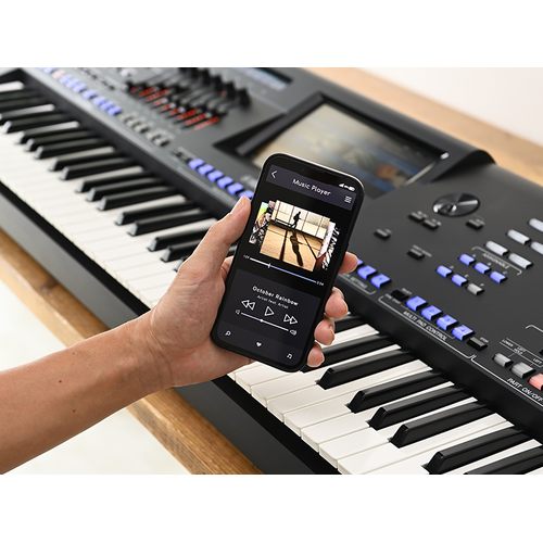 Genos2 and a hand holding a smartphone with a music player screen